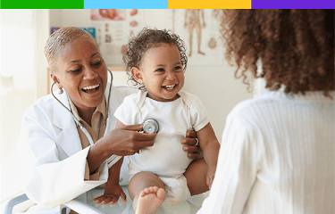 Actor portrayal of a young patient smiling at another person while a doctor applies a stethoscope